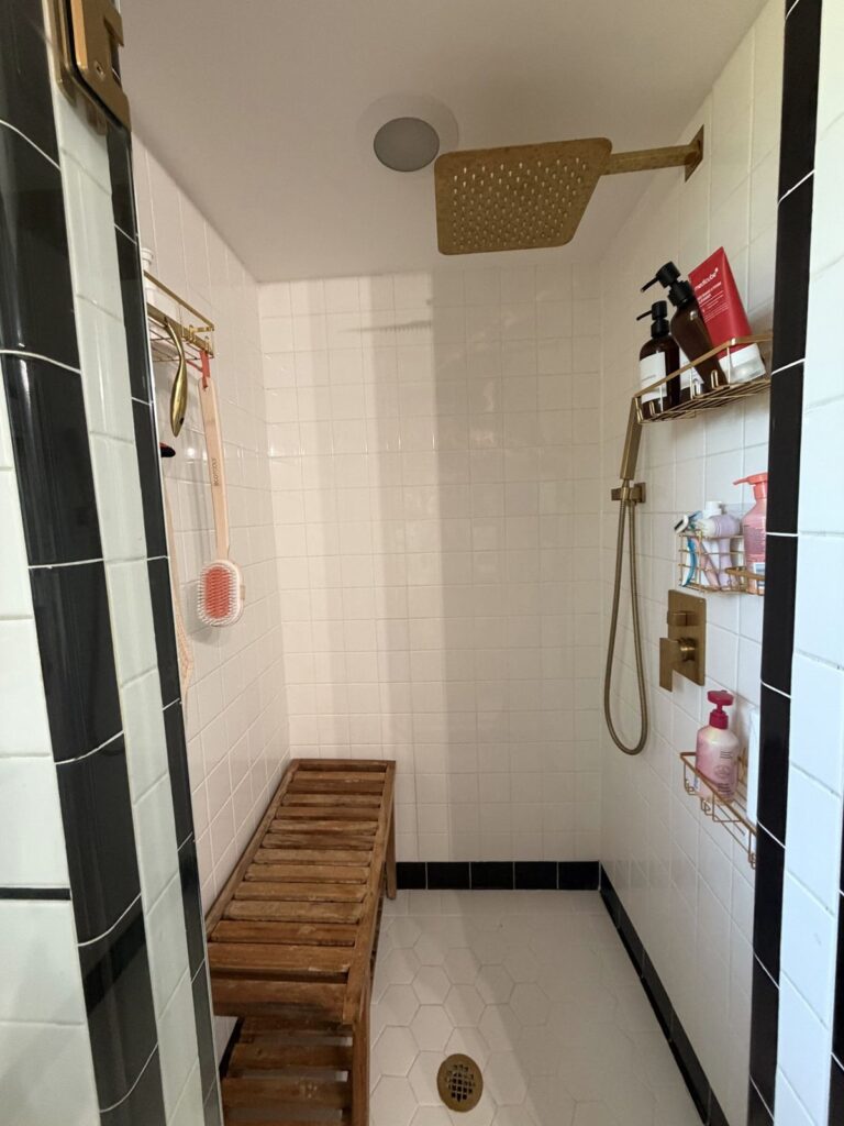 Before: separate tiled shower stall with brass rain head and wood bench