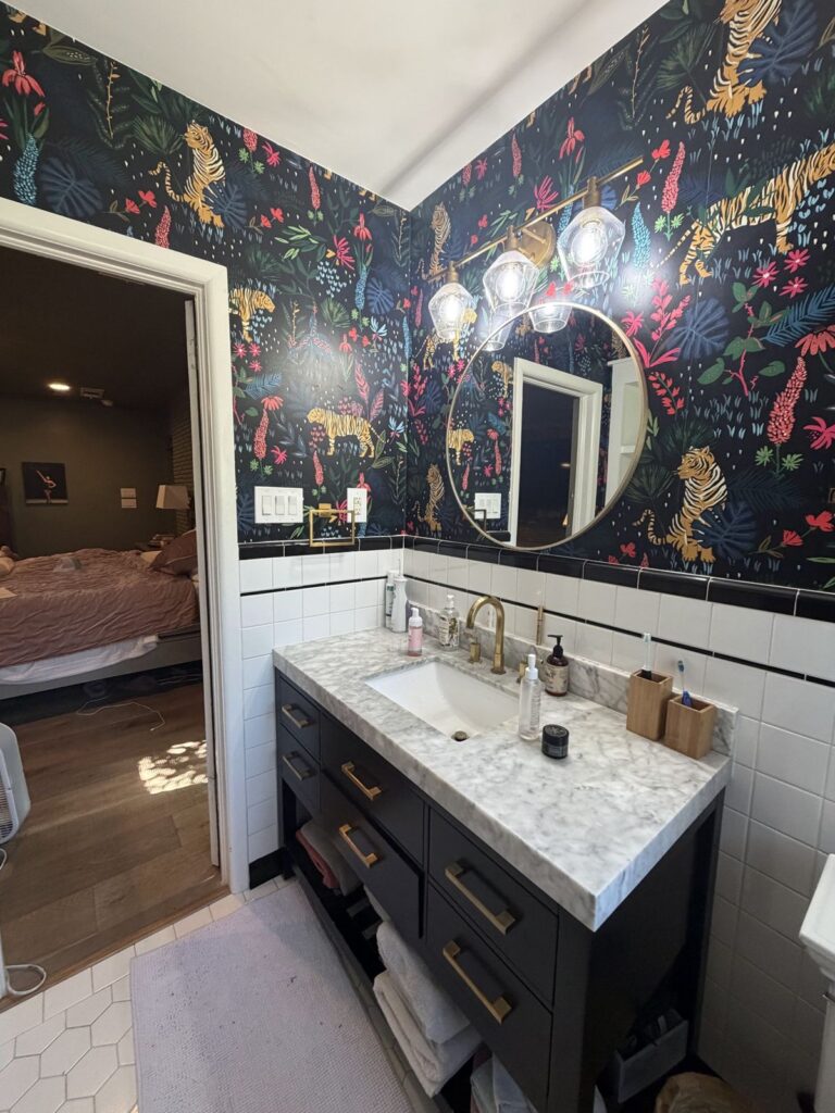 Before: vanity wall with dark tiger-print wallpaper and globe light fixture