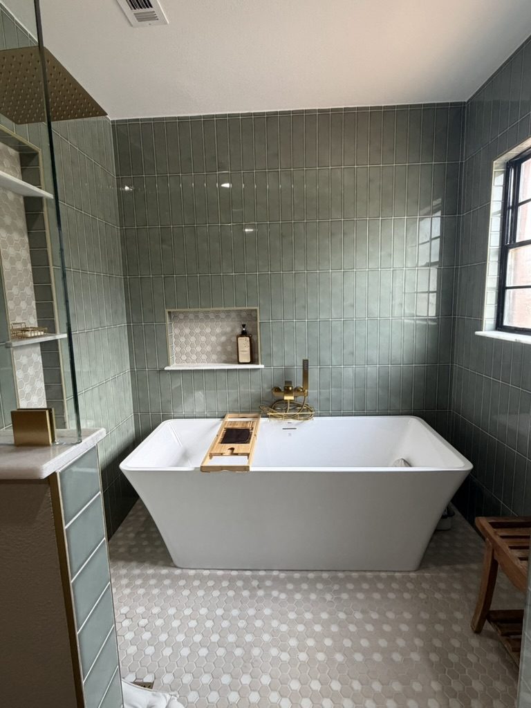 After: freestanding soaking tub with brass tub filler, recessed niche, and sage green vertical tile