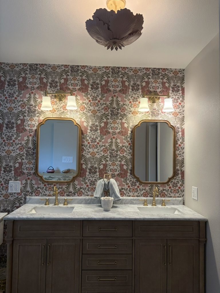 After: pair of gold scalloped mirrors with brass two-light sconces over a marble double vanity