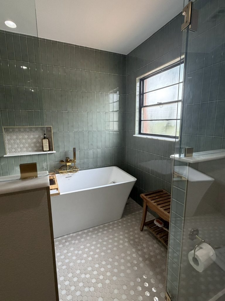 After: inside the wet room, a freestanding tub, teak bench, hex mosaic floor, and window in sage green tile